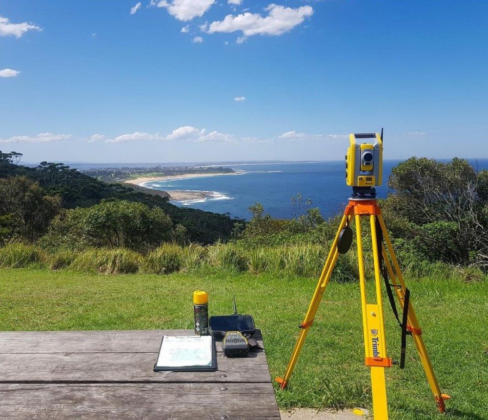 A total station set up on a coastal lookout, survey plans on the table