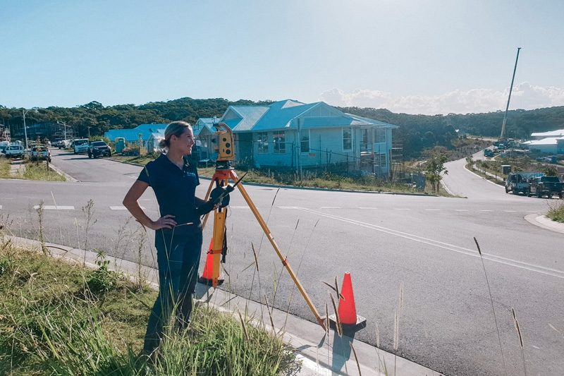 A Metiri surveyor working a total station beside a coastal creek